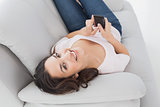 Smiling young woman text messaging on sofa at home
