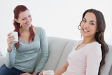 Young female friends with coffee cups sitting at home