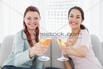 Happy female friends holding out wine glasses at home
