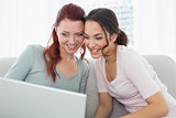 Happy young female friends using laptop at home
