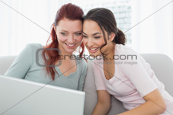 Happy young female friends using laptop at home