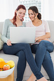 Relaxed young female friends using laptop at home