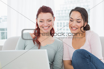Young female friends using laptop at home