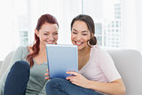 Cheerful relaxed friends using digital tablet at home