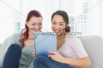 Cheerful relaxed friends using digital tablet at home