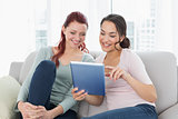 Happy relaxed female friends using digital tablet at home