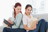 Female friends with digital tablet and book at home