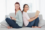 Female friends with digital tablet and book at home