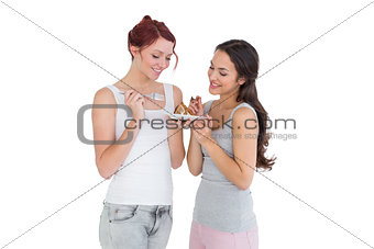 Two happy young female friends eating pastry together