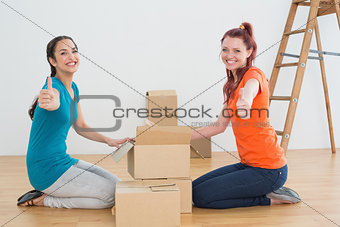 Female friends gesturing thumbs up with boxes in a new house
