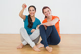 Female friends with house keys sitting on the floor