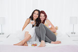 Happy young female friends with coffee cups in bed