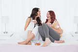 Cheerful female friends chatting over coffee in bed