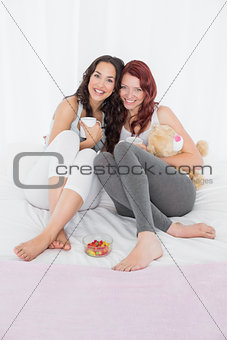 Happy young female friends with coffee cups in bed