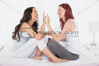 Happy female friends playing clapping game on bed