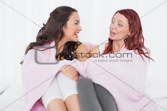 Female friends covered in sheet while chatting on bed
