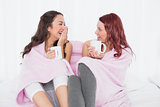 Cheerful relaxed friends chatting over coffee in bed