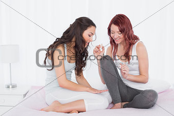 Pretty young woman painting friends nails on bed
