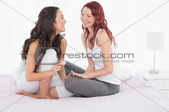 Pretty young woman painting friends nails on bed