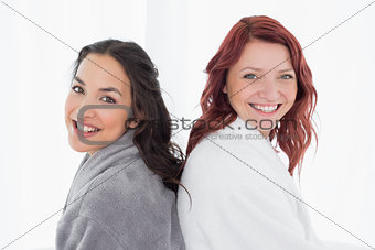 Female friends in bathrobes standing back to back