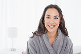 Happy young female in bathrobe sitting on bed