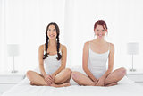 Happy female friends in white tank tops sitting on bed