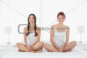 Happy female friends in white tank tops sitting on bed