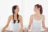 Two smiling women in white tank tops sitting on bed