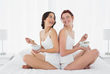 Two smiling female friends with bowls sitting on bed