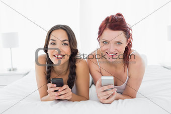 Relaxed smiling female friends text messaging on bed