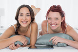 Two female friends with digital table lying in bed