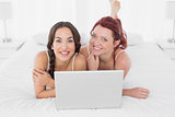 Relaxed smiling female friends with laptop in bed