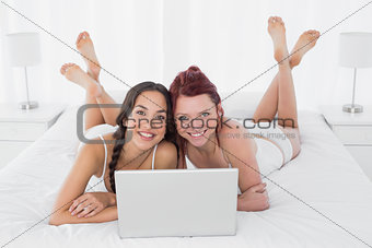 Relaxed smiling female friends with laptop in bed