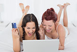 Cheerful female friends doing online shopping in bed