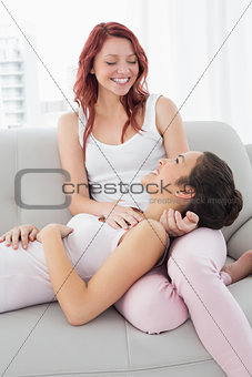 Happy female resting on friends lap in living room