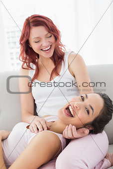 Cheerful young female resting on friends lap in living room