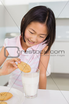 Smiling girl enjoying cookies and milk at home