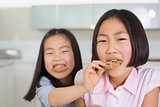 Girl feeding her elder sister a cookies in kitchen