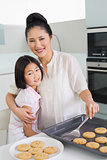 Mother hugging daughter while preparing cookies in kitchen