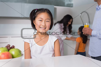 Smiling young girl with family in the background at kitchen