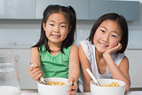 Portrait of two smiling girls sitting with bowls in kitchen