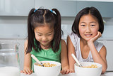 Two smiling young girls sitting with bowls in kitchen