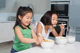 Two smiling young girls eating cereals in kitchen