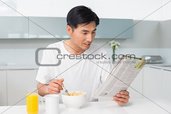 Young man having cereals while reading newspaper in kitchen