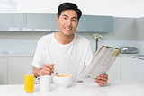 Smiling man having cereals while reading newspaper in kitchen