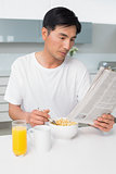 Serious man having cereals while reading newspaper in kitchen