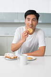Smiling young man having biscuits and coffee in kitchen