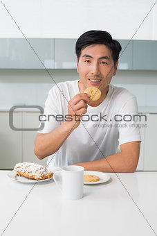 Smiling young man having biscuits and coffee in kitchen