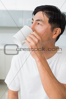 Serious man drinking coffee as he looks away in kitchen