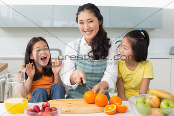 Woman with cheerful two daughters cutting fruit in kitchen